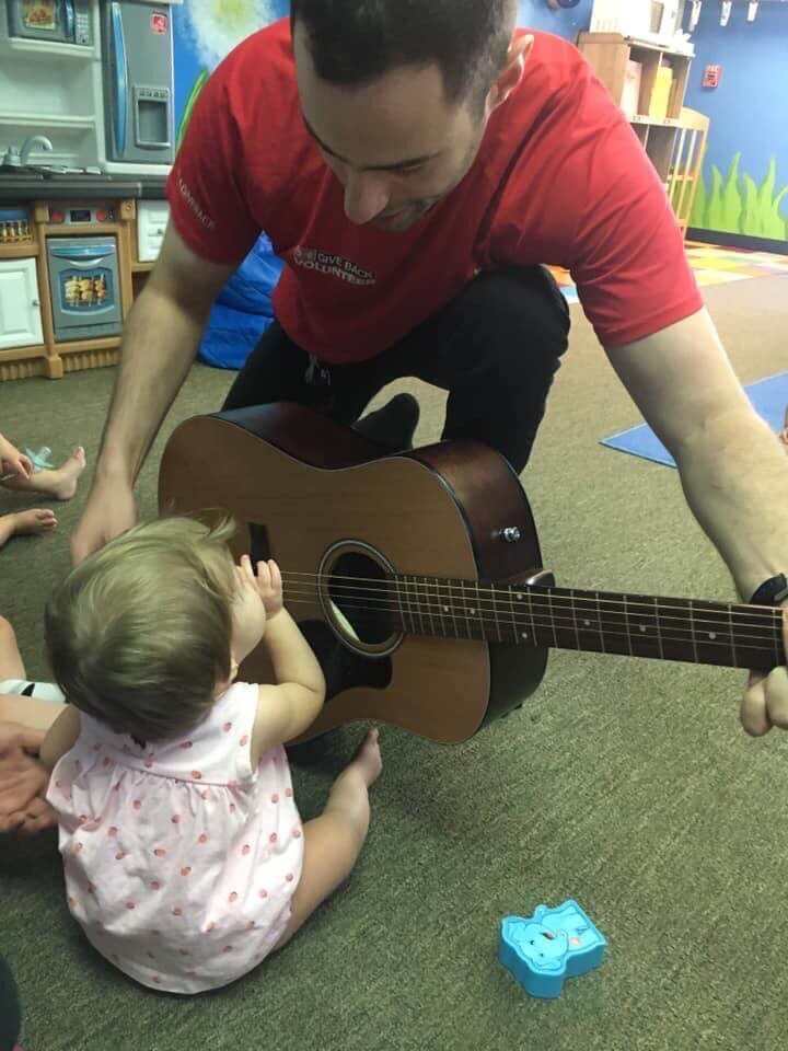 Teacher holding a guitar and an infant playing the guitar. Visit our Cockeysville, Maryland preschool education center.