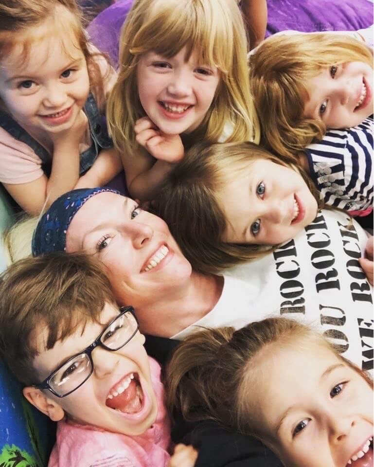 six kids and a teacher smiling in the camera